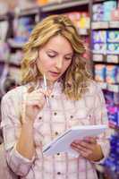 Smiling pretty blonde woman writing on her notepad and thinking