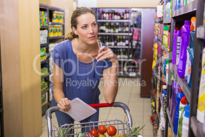 Pretty woman looking at product on shelf and holding grocery lis