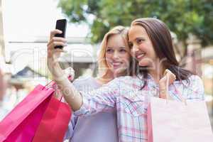 Happy women friends taking a selfie and holding shopping bags