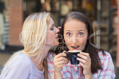 Blonde woman telling secret to her friend while drinking coffee