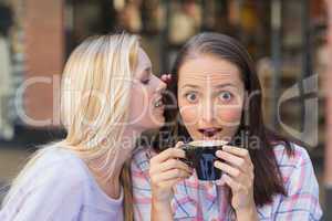 Blonde woman telling secret to her friend while drinking coffee