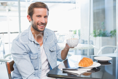 Young happy man smiling at the camera and holding coffee in his