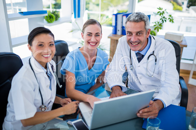 Doctors and nurse looking at laptop and smiling at camera