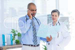 Concentrated doctor showing file to his colleague while calling