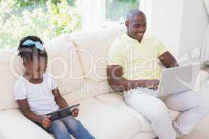 Happy smiling father using laptop and her daughter using tablet