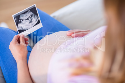 Pregnant woman looking at ultrasound scans and touching her bell