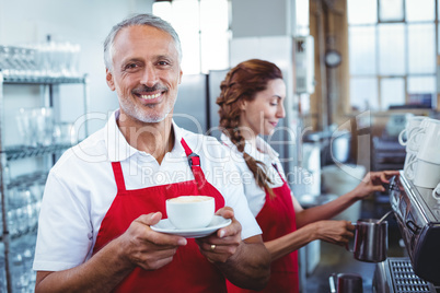 Happy barista smiling at camera and holding a cup of coffee