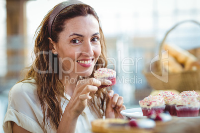Pretty brunette looking at camera and holding cupcake