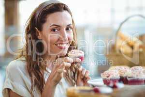 Pretty brunette looking at camera and holding cupcake