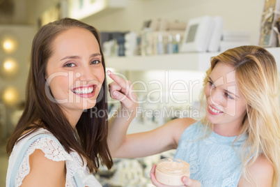 Happy blonde woman applying cosmetic products on her friend