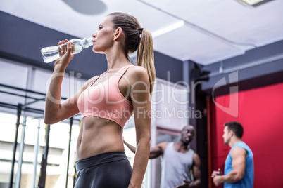 Young woman drinking water from a bottle with colleagues behind