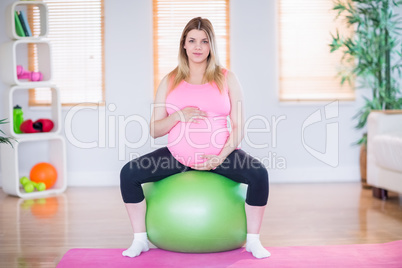 Pregnant woman looking at camera sitting on exercise ball