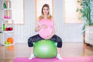 Pregnant woman looking at camera sitting on exercise ball