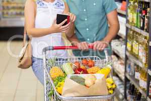 Smiling bright couple buying food products and using notebook