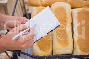 A woman writing a grocery list above bread loaf