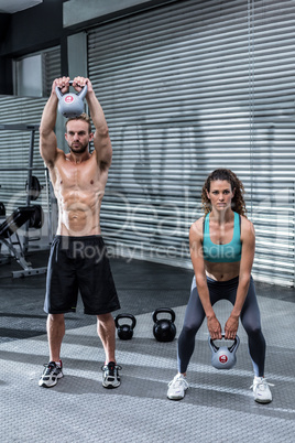 A muscular couple lifting kettlebells