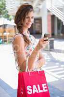 Smiling woman with sale shopping bags using smartphone