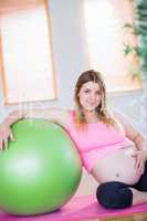 Pregnant woman looking at camera next to exercise ball