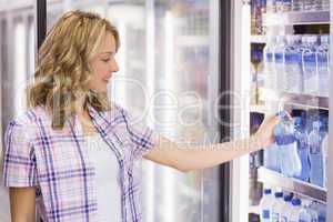 Smiling pretty blonde woman taking a water bottle in supermarket