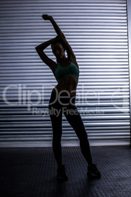 Muscular woman stretching in shadow room