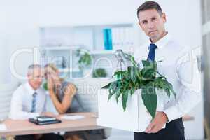 Businessman carrying his belongings with colleagues behind