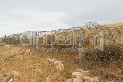 Barbed tape or razor wire fence across the desert hill on cloudy day