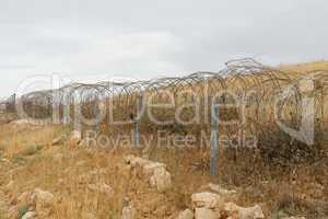 Barbed tape or razor wire fence across the desert hill on cloudy day