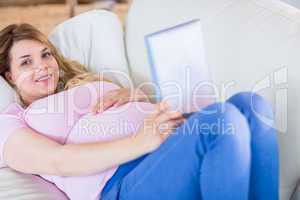 Smiling pregnant woman looking at camera and using tablet