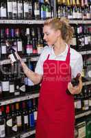 Smiling blonde worker looking at a wine bottle
