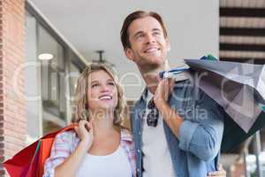 A smiling couple with shopping bags looking away