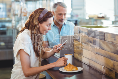 Pretty brunette using her smartphone with coffee in her hand