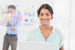 Businesswoman presenting laptop screen with colleague behind her