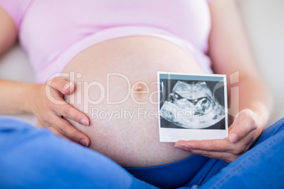 Pregnant woman showing ultrasound scans and touching her belly