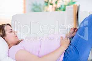 Pregnant woman reading a book on couch