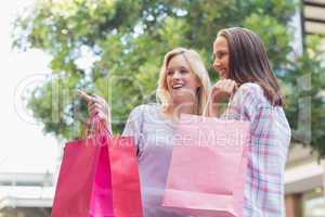 Happy women with shopping bags and pointing away