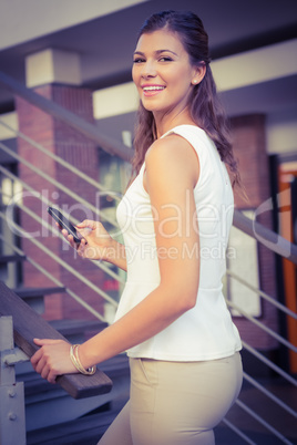 Portrait of smiling woman going upstairs while using her smartph