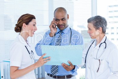 Concentrated doctor showing file to his colleagues while calling