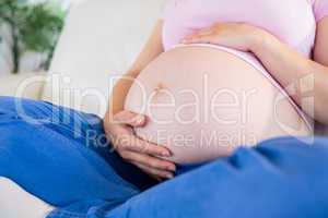 Close up of pregnant woman sitting on couch touching her belly