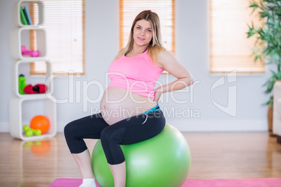 Pregnant woman looking at camera sitting on exercise ball