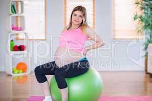 Pregnant woman looking at camera sitting on exercise ball