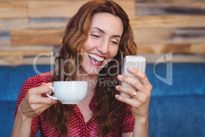 Woman using her mobile phone and holding cup of coffee