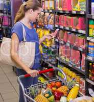 Pretty woman using her smartphone in front of product on shelf