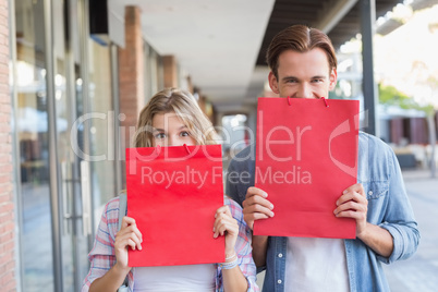 A happy couple hiding themselves behind red bags