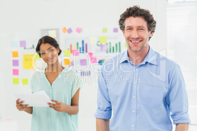 Happy businessman looking at camera with colleague behind