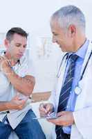 Doctor examining his patient and writing on clipboard