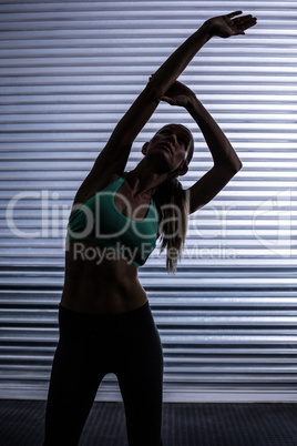 Muscular woman stretching in shadow room