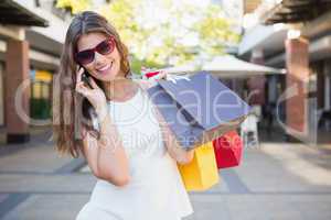 Smiling woman with sunglasses and shopping bags calling