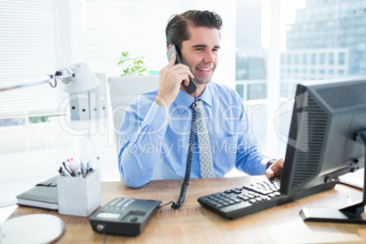 Smiling businessman using his computer ans phoning