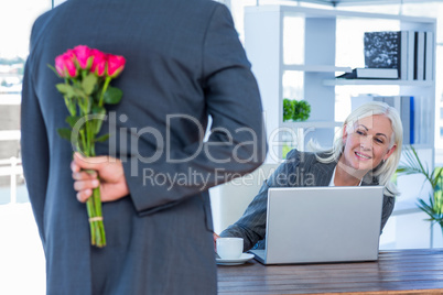 Businessman hiding flowers behind back for colleague