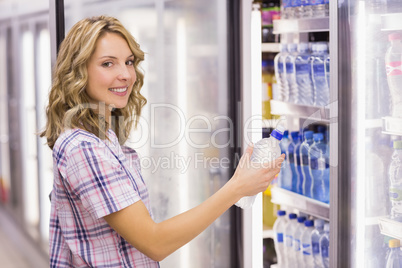 Portrait of a smiling pretty blonde woman taking a water bottle